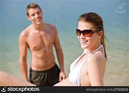 Woman in bikini sunbathing by sea on beach, man in background