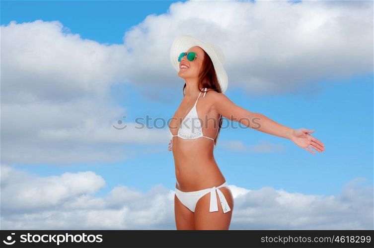Woman in bikini with arms outstretched with a nice background of a blue sky with clouds
