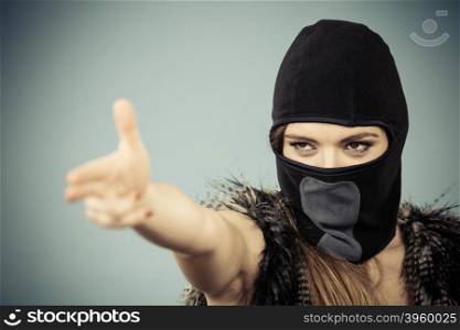 Woman in black balaclava making gun gesture. Crime and violence on blue studio shot