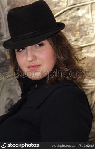 Woman in black felt hat lean-to the stone wall