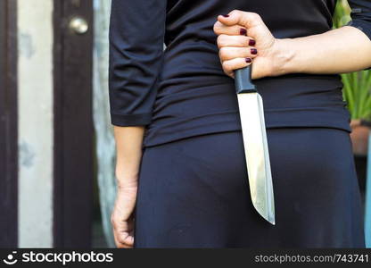 Woman in black holding a knife hidden behind.