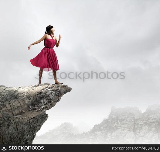 Woman in blindfold. Woman in red dress standing on edge of rock