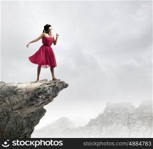 Woman in blindfold. Woman in red dress standing on edge of rock