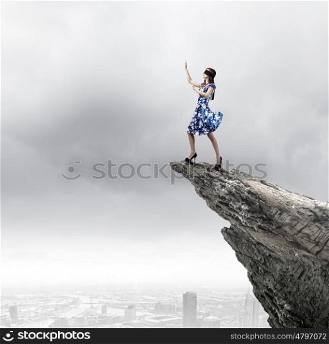 Woman in blindfold. Young woman in blue dress standing on mountain edge