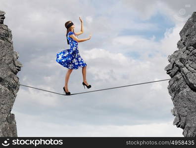 Woman in blindfold. Young woman in blue dress standing on mountain edge