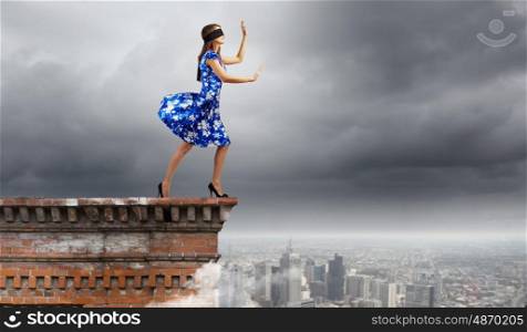Woman in blindfold. Young woman in blue dress standing on roof edge