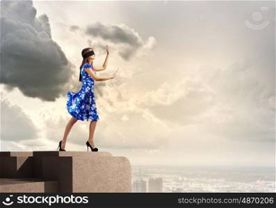 Woman in blindfold. Young woman in blue dress standing on roof edge