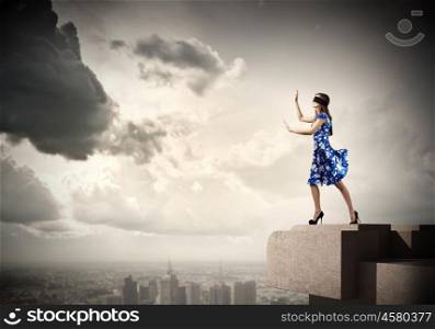 Woman in blindfold. Young woman in blue dress walking on edge of roof