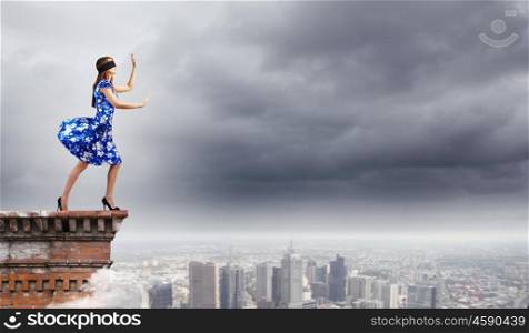 Woman in blindfold. Young woman in blue dress walking on edge of roof