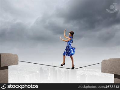 Woman in blindfold. Young woman in blue dress walking on rope above gap
