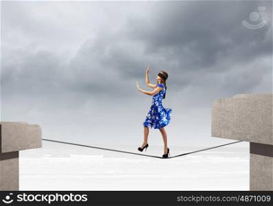 Woman in blindfold. Young woman in blue dress walking on rope above gap