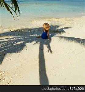 Woman in blue dress on a tropical beach at Maldives sitting in palm tree shadow