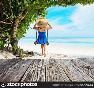 Woman in blue dress swinging at tropical beach