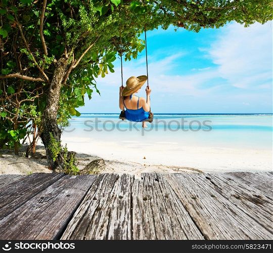 Woman in blue dress swinging at tropical beach