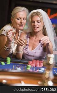 Woman in bridal veil with another woman in casino playing roulette and smiling (selective focus)