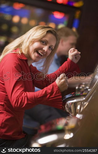 Woman in casino excited playing slot machine with people in background (selective focus)