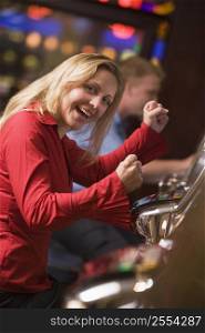 Woman in casino excited playing slot machine with people in background (selective focus)