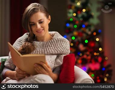 Woman in chair in front of Christmas tree reading book