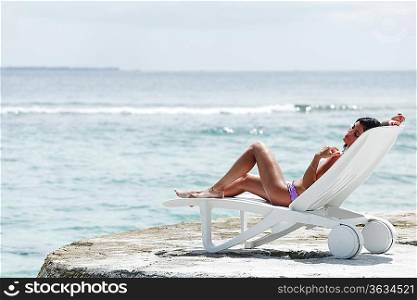 Woman in chaise-lounge near sea