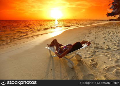 Woman in chaise-lounge relaxing on beach