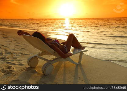 Woman in chaise-lounge relaxing on beach