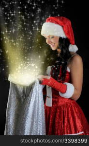 Woman in christmas hat smiles and holding a gift in magic bag on a dark background