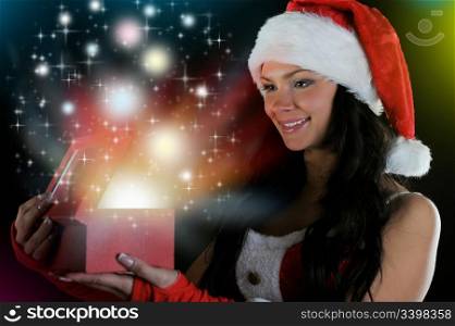 Woman in christmas hat smiles and holding a gift in magic packing on a dark background