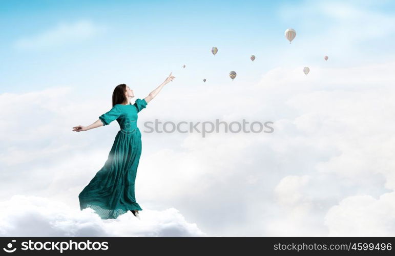 Woman in cloudy sky. Elegant woman in green long dress walking on clouds