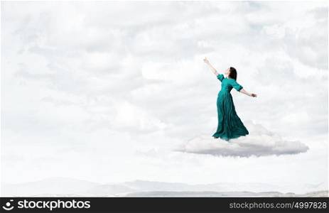 Woman in cloudy sky. Elegant woman in green long dress walking on clouds