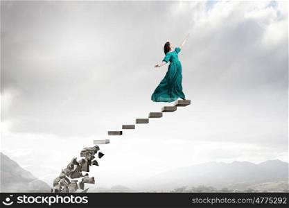 Woman in cloudy sky. Elegant woman in green long dress walking on steps
