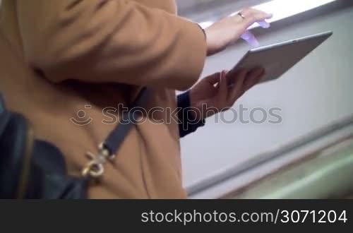 Woman in coat walking fast upstairs in underground and using tablet computer