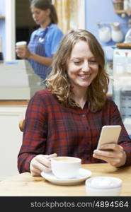 Woman In Coffee Shop Reading Text Message On Mobile Phone