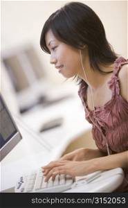 Woman in computer room listening to MP3 player while typing and smiling