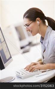Woman in computer room listening to MP3 Player while typing and smiling