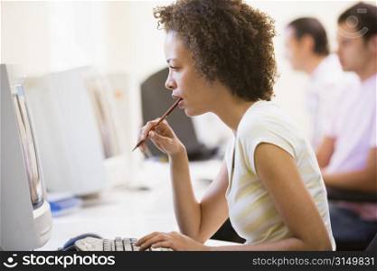 Woman in computer room looking at monitor and thinking