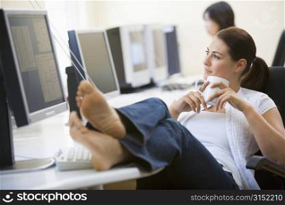 Woman in computer room with feet up drinking coffee