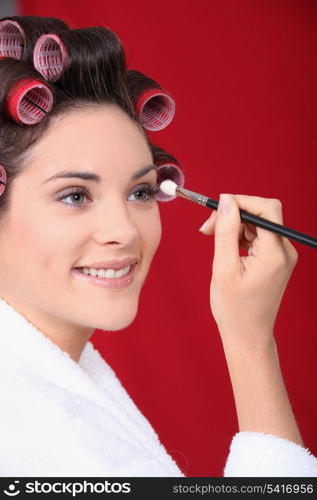 Woman in curlers applying eyeshadow