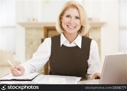 Woman in dining room with laptop and paperwork smiling