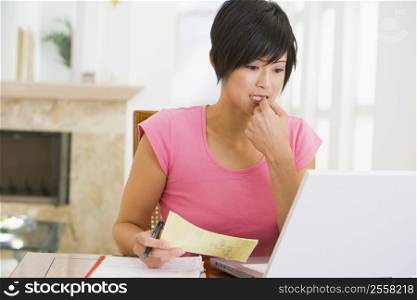 Woman in dining room with laptop thinking