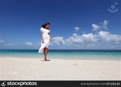 Woman in dress on beach. Beautiful young woman in white dress walking on beach