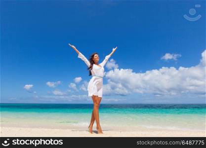 Woman in dress on beach. Woman in white dress posing in tropical sea beach with arms raised