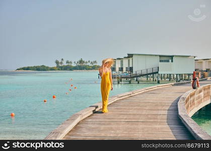 Woman in dress walking on tropical beach boardwalk. Summer vacation at Maldives.