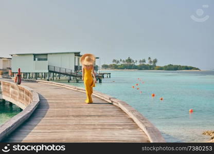 Woman in dress walking on tropical beach boardwalk. Summer vacation at Maldives.