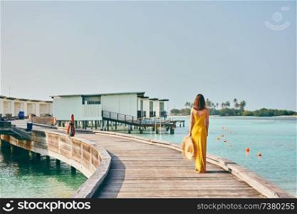Woman in dress walking on tropical beach boardwalk. Summer vacation at Maldives.