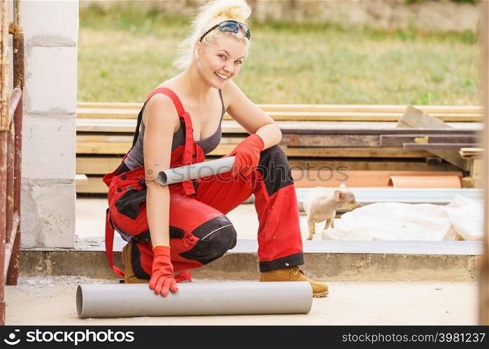 Woman in dungarees carrying and installing plastic pipes on her home construction site, building new home.. Woman installing pipes on construction site