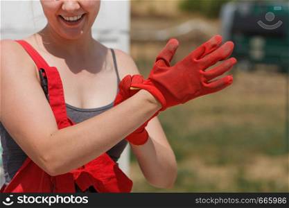 Woman in dungarees putting on red industrial safety worker gloves about to do work on construction site.. Woman putting safety worker gloves