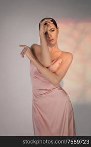 Woman in elegant fashionable dress. Beautiful model pose in studio in pink evening clothes. Classic silk dress. Sexy lady stay on white background. Perfect young woman with classic hairstyle and makeup.