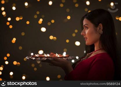 Woman in ethnic attire holding a plate full of diyas in her hands