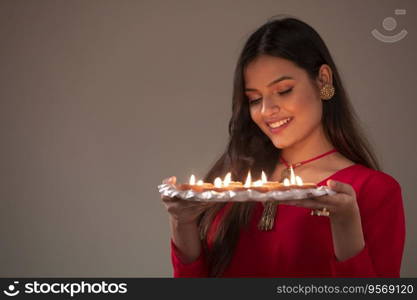 Woman in ethnic attire looking at a plate full of diyas in her hand