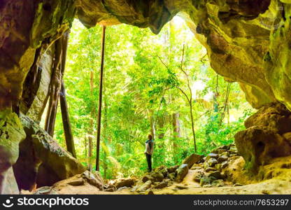Woman in exit of dark cave or grotto to light green tropical forest
